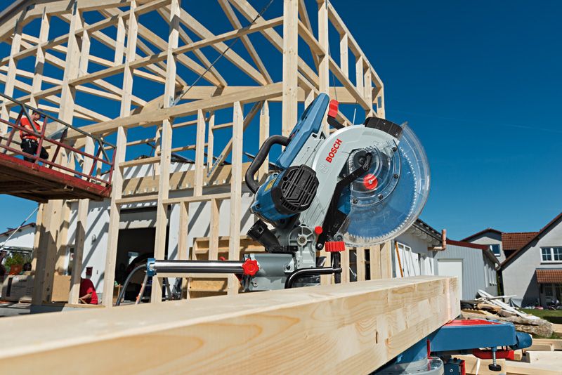 Auf einer Hausbaustelle ist eine Kapp- und Gehrungssäge auf einem Holzbalken positioniert.