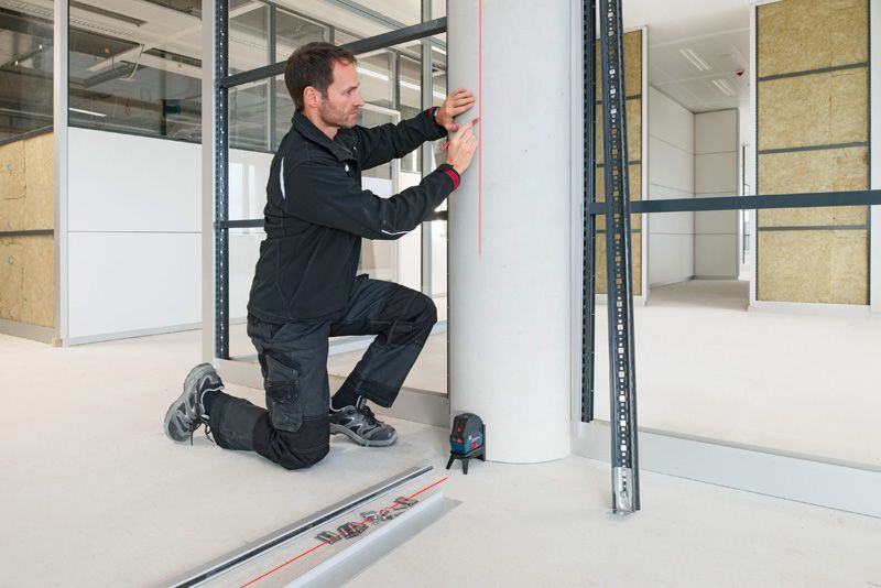 Eine Person mit Sicherheitsausrüstung markiert eine Säule mit einem Lasernivelliergerät.