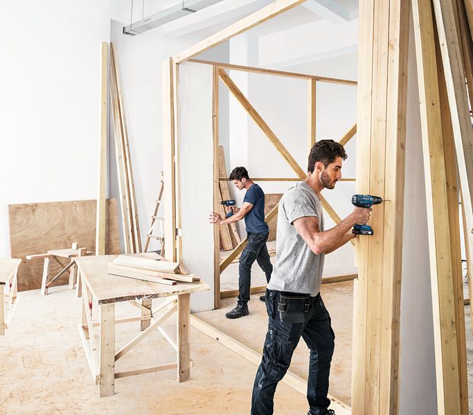 Zwei Männer bauen eine Holzmauer.
