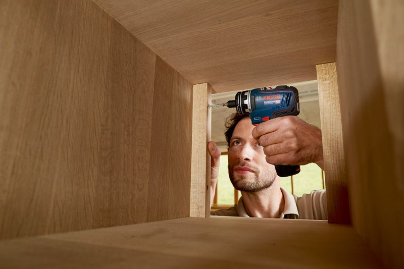 Eine Person verwendet eine Akkubohrmaschine, um einen Holzschrank zusammenzubauen.