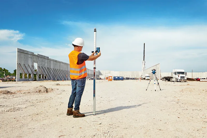 Eine Person mit Sicherheitsausrüstung verwendet auf einer Baustelle ein Lasernivelliergerät.