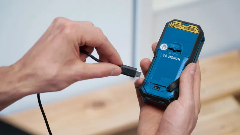 Eine Person schließt ein Ladekabel an der Rückseite eines handgeführten Elektrowerkzeugs an.