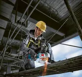 Eine Person mit Schutzausrüstung schneidet mit einem Winkelschleifer Metallträger.