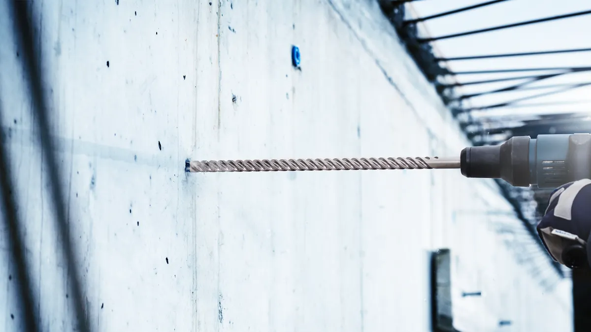Person mit Schutzausrüstung bohrt mit Bohrhammer in eine Betonwand.