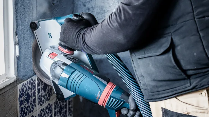 Eine Person mit Schutzausrüstung bedient einen Mauerwerksschleifer mit Staubabsaugung.