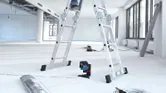Ein Laser-Nivelliergerät projiziert rote Linien auf den Boden in einem hellen, unfertigen Raum.