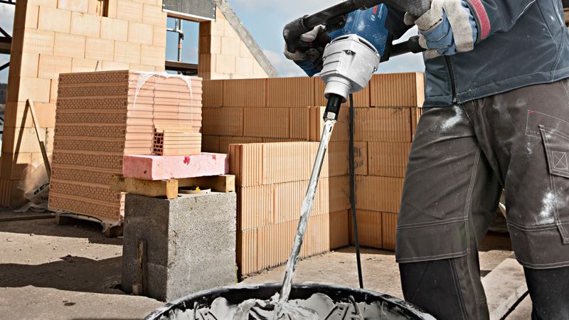 Eine Person mit Sicherheitsausrüstung mischt auf einer Baustelle Zement mit einem Rührwerk.