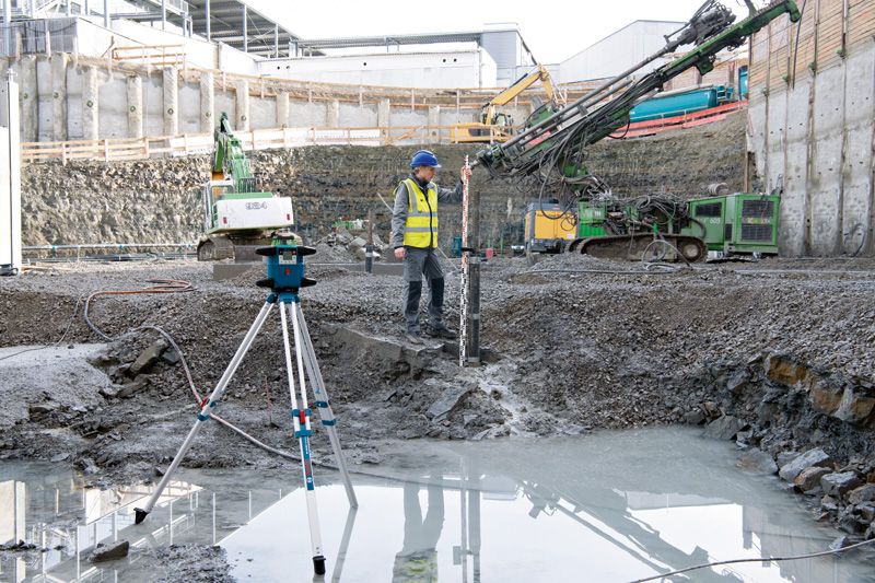 Eine Person mit Sicherheitsausrüstung verwendet auf einer Baustelle ein Lasernivelliergerät.