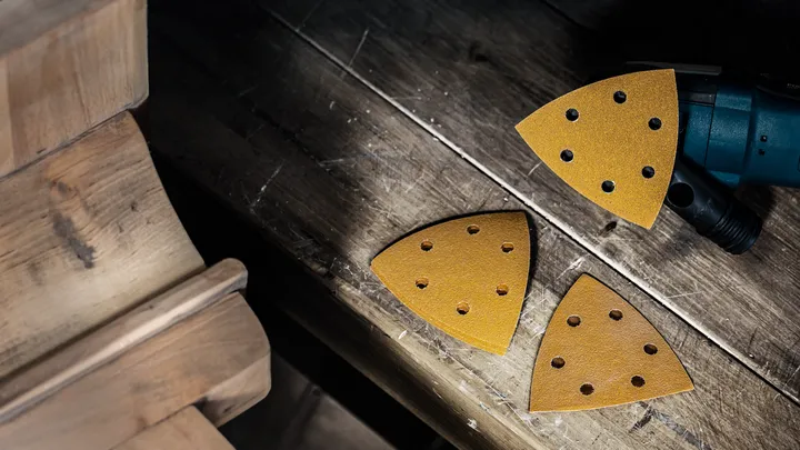 Detailschleifer mit dreieckigen Schleifpapierpads auf einer Holzwerkbank.