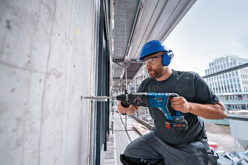 Eine Person mit Schutzausrüstung bohrt mit einem Akku-Bohrhammer in Beton.