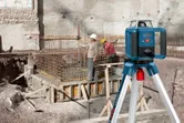 Ein Arbeiter in Schutzausrüstung benutzt auf einer Baustelle ein Laser-Nivelliergerät.