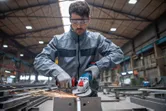 Eine Person, die Schutzausrüstung trägt, schleift in einer Fabrik Metall mit einem Akku-Winkelschleifer.