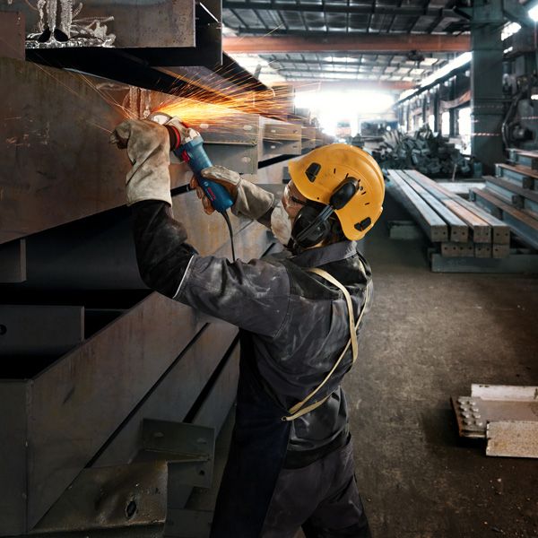 Eine Person mit Schutzausrüstung schleift einen Metallstrahl und erzeugt dabei helle Funken.