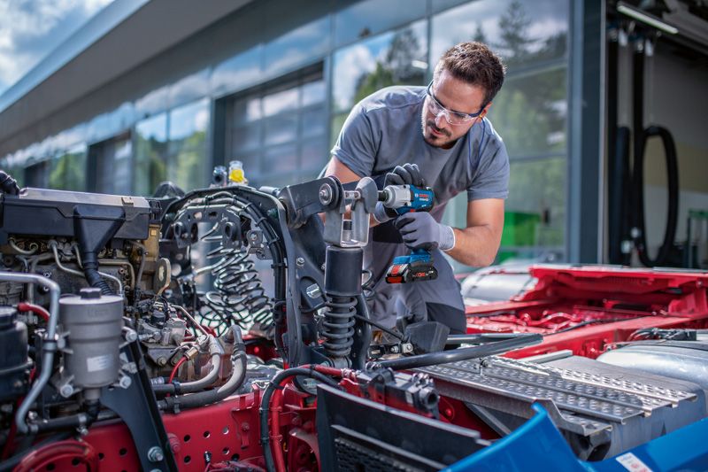 Eine Person mit Sicherheitsausrüstung verwendet einen Akku-Schlagschrauber an einem Fahrzeugchassis.