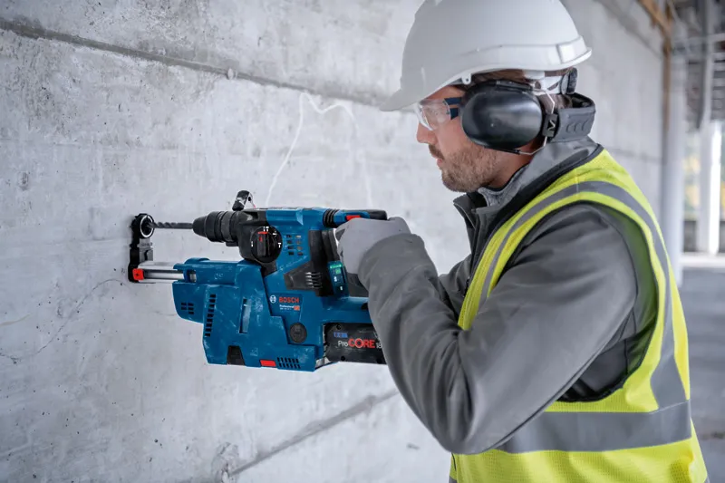 Eine Person mit Schutzausrüstung bohrt mit einem Bohrhammer in eine Betonwand.