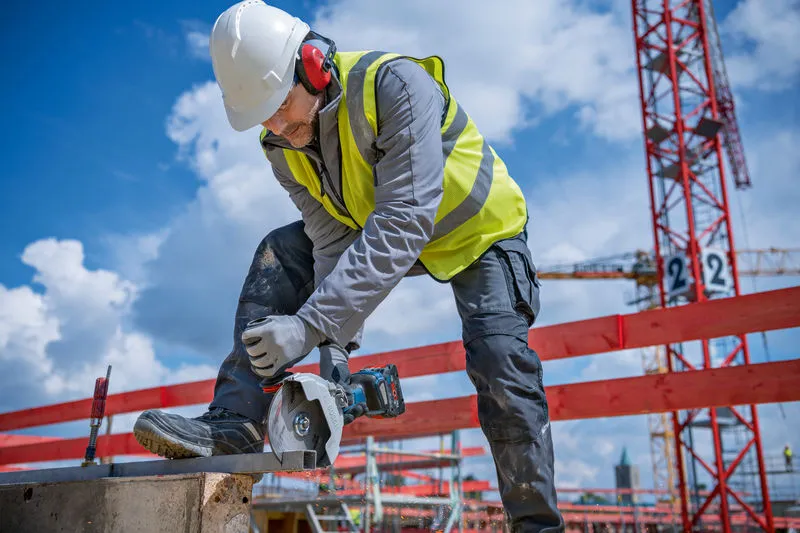 Eine Person mit Schutzausrüstung schneidet auf einer Baustelle Metall mit einem Akku-Winkelschleifer.
