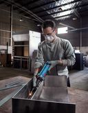 Eine Person mit Sicherheitsausrüstung schleift Metall in einer Industriewerkstatt.