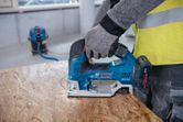 Eine Person, die Schutzausrüstung trägt, benutzt eine Akku-Stichsäge, um Holzpaneele zuzuschneiden.