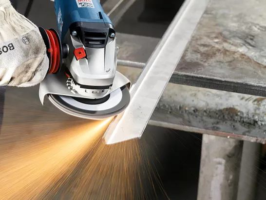 Ein Arbeiter mit Sicherheitsausrüstung schleift eine Metallstange mit einem Winkelschleifer.