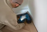Eine Person, die Schutzausrüstung trägt, befestigt mit einem kabellosen Druckluftnagler Fußleisten.