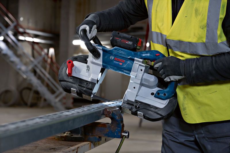 Eine Person mit Schutzausrüstung schneidet einen Metallträger mit einer Akku-Bandsäge.