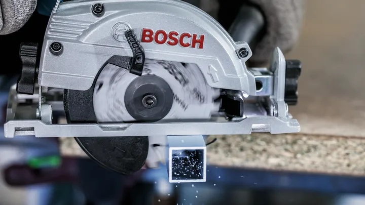 Eine Person mit Sicherheitsausrüstung schneidet mit einer Kreissäge ein Vierkantrohr aus Metall.