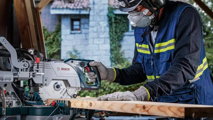 Eine Person mit Sicherheitsausrüstung schneidet Holz mit einer Motorsäge.