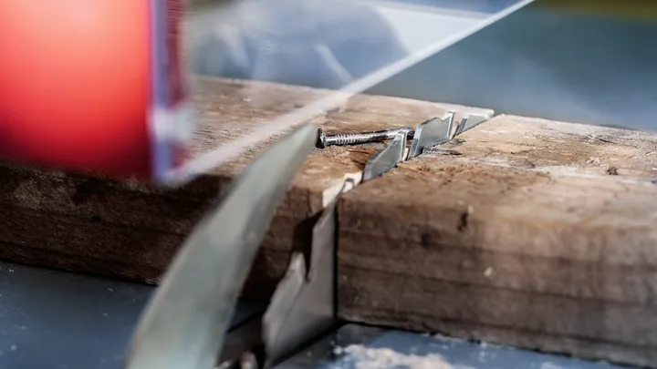 Eine Kreissäge schneidet durch ein Holzbrett mit einer eingebetteten Metallschraube.
