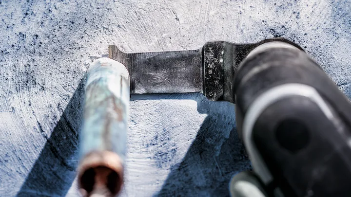 Oszillierendes Werkzeug schneidet durch ein Metallrohr auf einer Betonoberfläche.