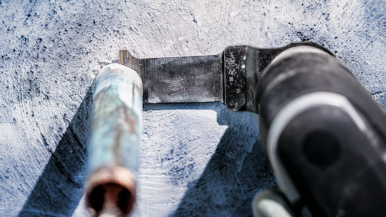 Oszillierendes Werkzeug schneidet durch ein Metallrohr auf einer Betonoberfläche.