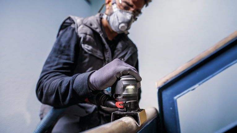 Eine Person mit Sicherheitsausrüstung schleift mit einem Elektrowerkzeug ein Metallgeländer.