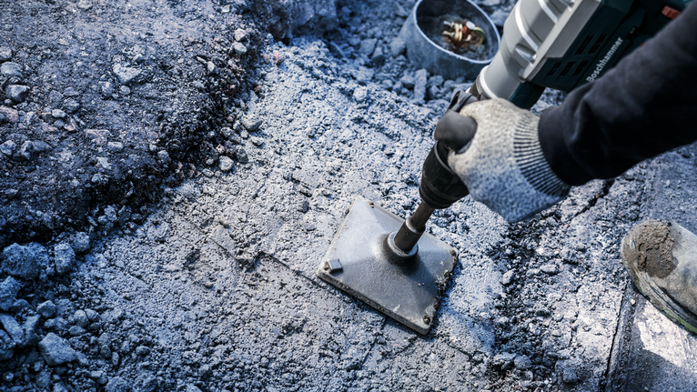 Eine Person mit Sicherheitsausrüstung bricht Beton mit einem Hochleistungs-Elektrowerkzeug.