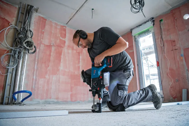Eine Person mit Schutzausrüstung bohrt mit einem Akku-Bohrhammer in einen Betonboden.