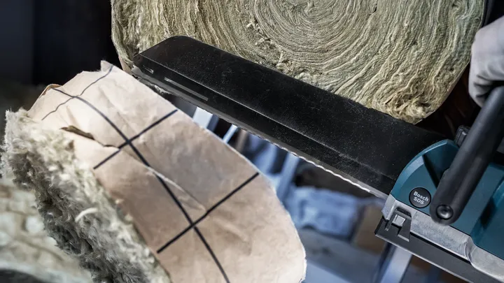 Person mit Schutzausrüstung schneidet Dämmmaterial mit einer Motorsäge.