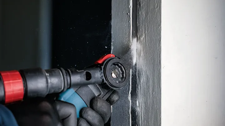 Eine Person mit Sicherheitsausrüstung schneidet mit einem Elektrowerkzeug in einen Türrahmen.