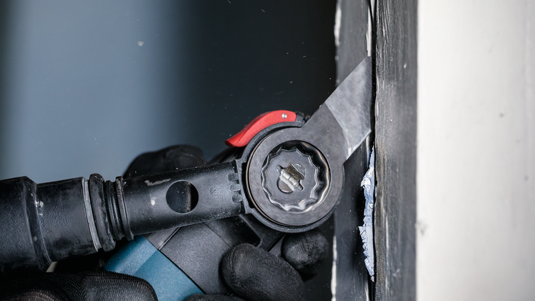 Eine Person mit Sicherheitsausrüstung verwendet ein Elektrowerkzeug, um Material in der Nähe einer Wand zu schneiden.