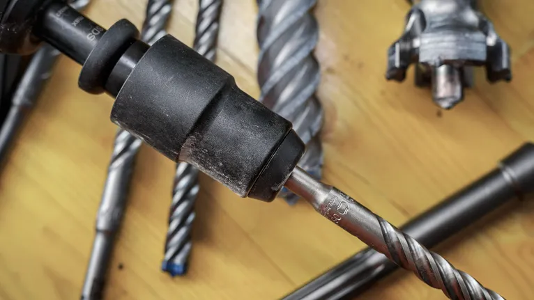 Nahaufnahme verschiedener Metallbohrer und eines Bohrfutters auf einer Holzoberfläche.