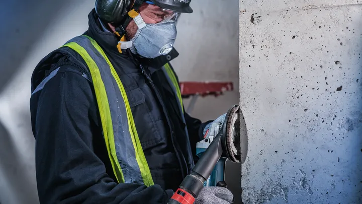 Arbeiter in Sicherheitsausrüstung schleift Betonwand mit Elektrowerkzeug.
