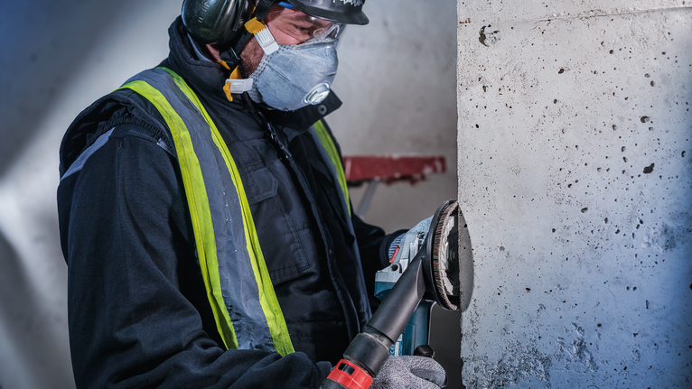 Arbeiter in Sicherheitsausrüstung schleift Betonwand mit Elektrowerkzeug.