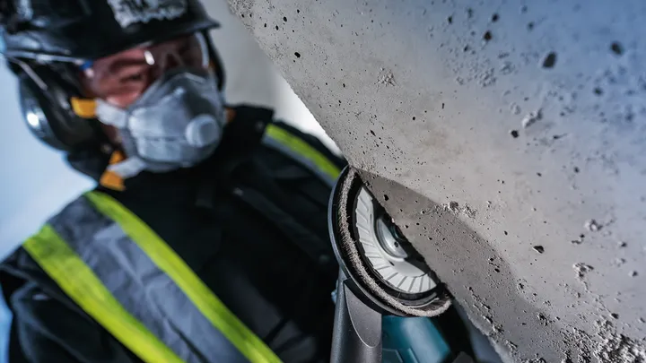 Eine Person mit Sicherheitsausrüstung schleift eine Betonoberfläche mit einem Elektrowerkzeug.