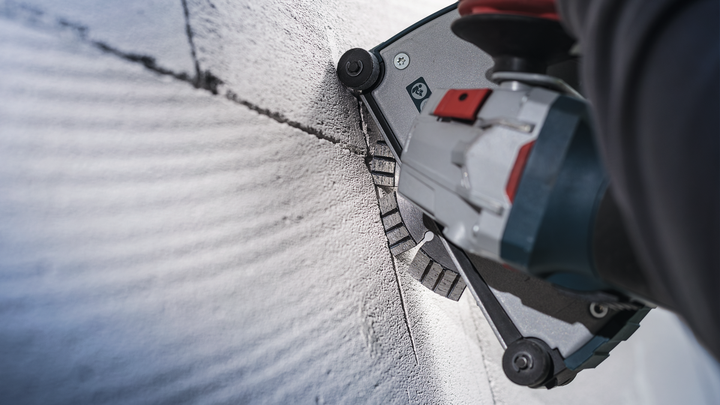 Eine Person mit Sicherheitsausrüstung schneidet mit einem Elektrowerkzeug eine Nut in eine Betonwand.