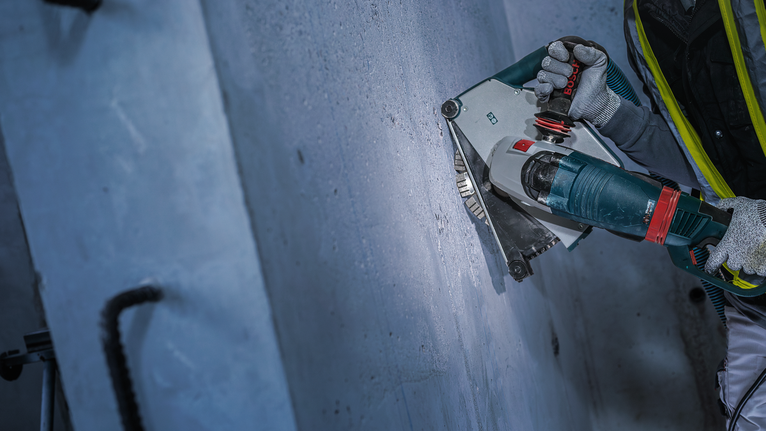 Eine Person mit Sicherheitsausrüstung schneidet mit einem Elektrowerkzeug eine Nut in eine Betonwand.