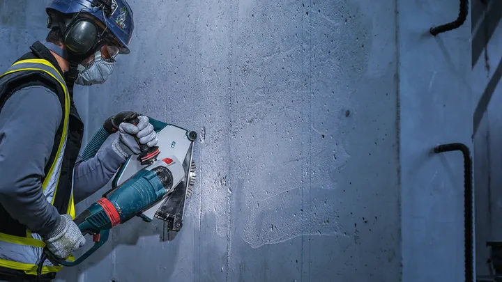 Eine Person mit Sicherheitsausrüstung schneidet mit einem Elektrowerkzeug in eine Betonwand.