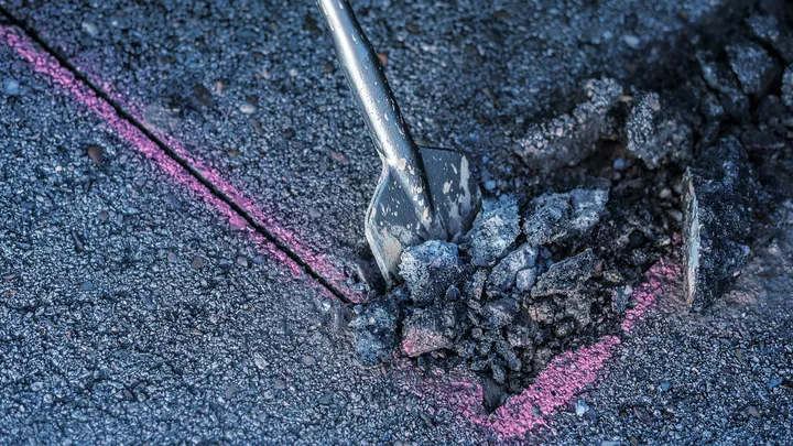 Meißel bricht Asphalt entlang einer rosafarbenen Markierung.