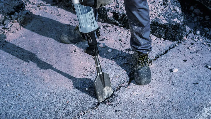 Eine Person mit Sicherheitsausrüstung zertrümmert Beton mit einem Abbruchhammer.