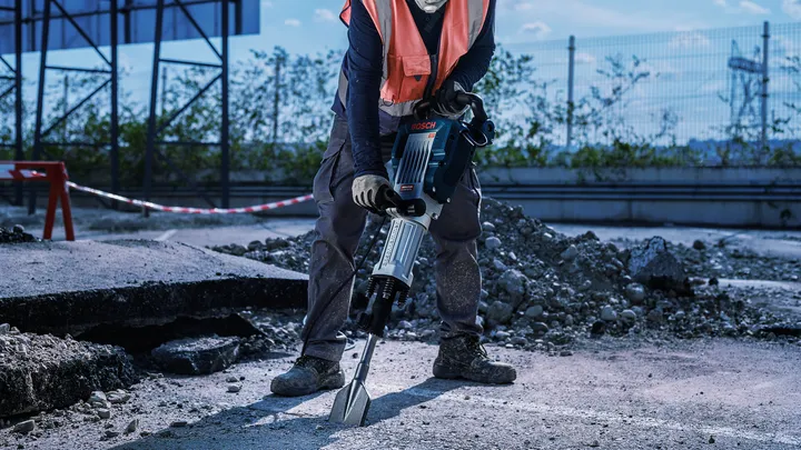 Eine Person mit Sicherheitsausrüstung verwendet einen Abbruchhammer, um Beton aufzubrechen.