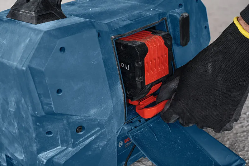 Eine Person mit Sicherheitsausrüstung legt eine Batterie in ein blaues Baustellenradio ein.