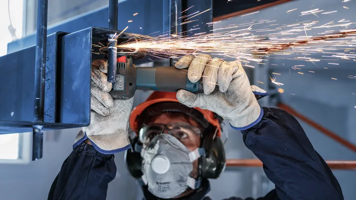 Eine Person mit Sicherheitsausrüstung schleift Metall und erzeugt Funken.