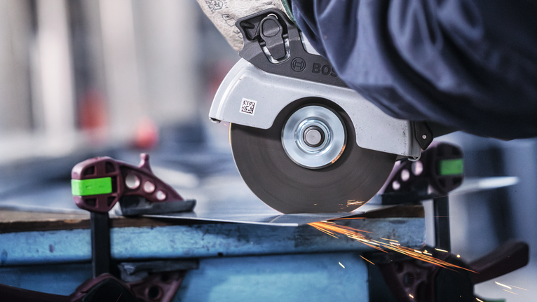 Eine Person mit Schutzausrüstung schneidet mit einer Kreissäge ein Metallblech, wobei Funken entstehen.