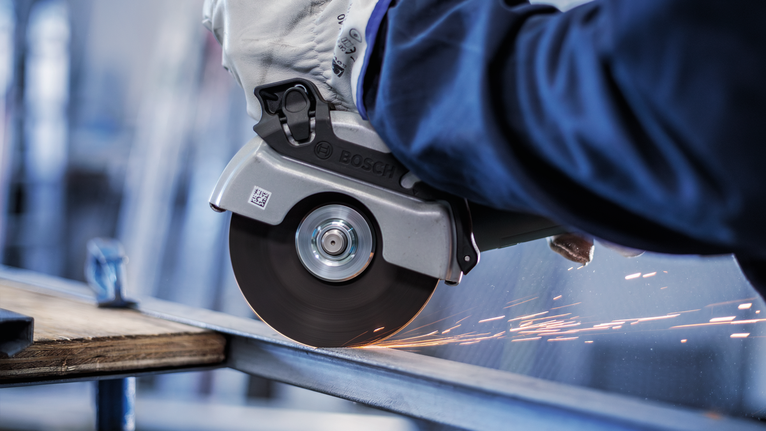 Eine Person mit Sicherheitsausrüstung verwendet einen Winkelschleifer, um einen Metallträger zu schneiden.